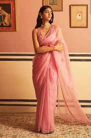 Woman wearing a pink saree paired with traditional jewellery and a stylish side-parted hairstyle, standing indoors in an elegant setting.