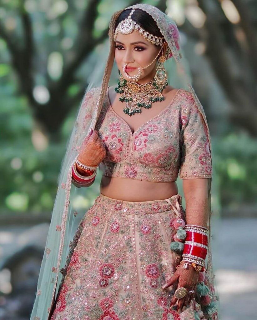 Bride in a pastel lehenga adorned with heavy maangtikka and traditional jewellery, showcasing elegant bridal style.